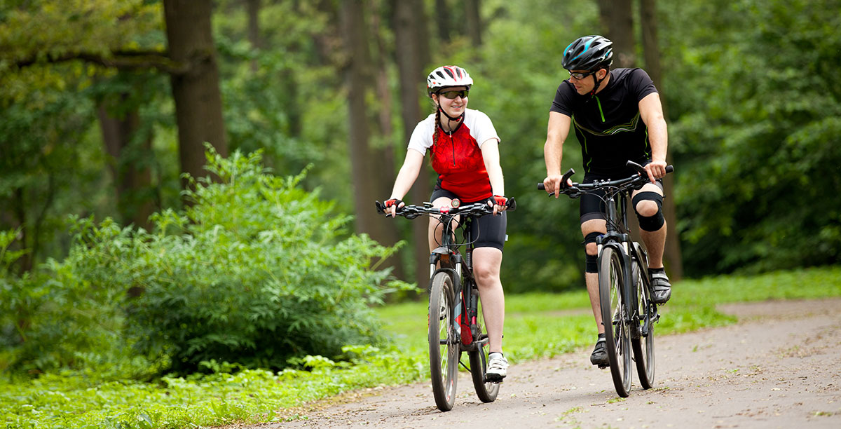 Uomo e donna in bicicletta su una strada sterrata nel mezzo del bosco