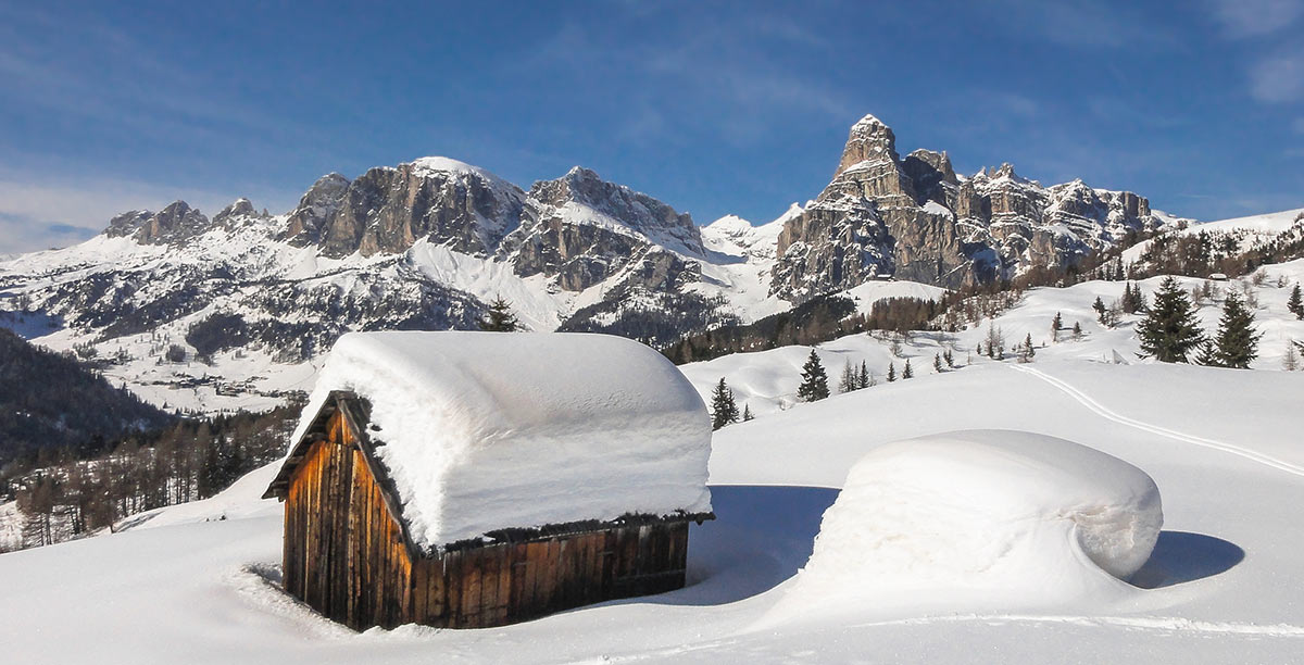 Holzhütte mit einem Meter Schnee auf dem Dach und die Berge von Alta Badia im Hintergrund