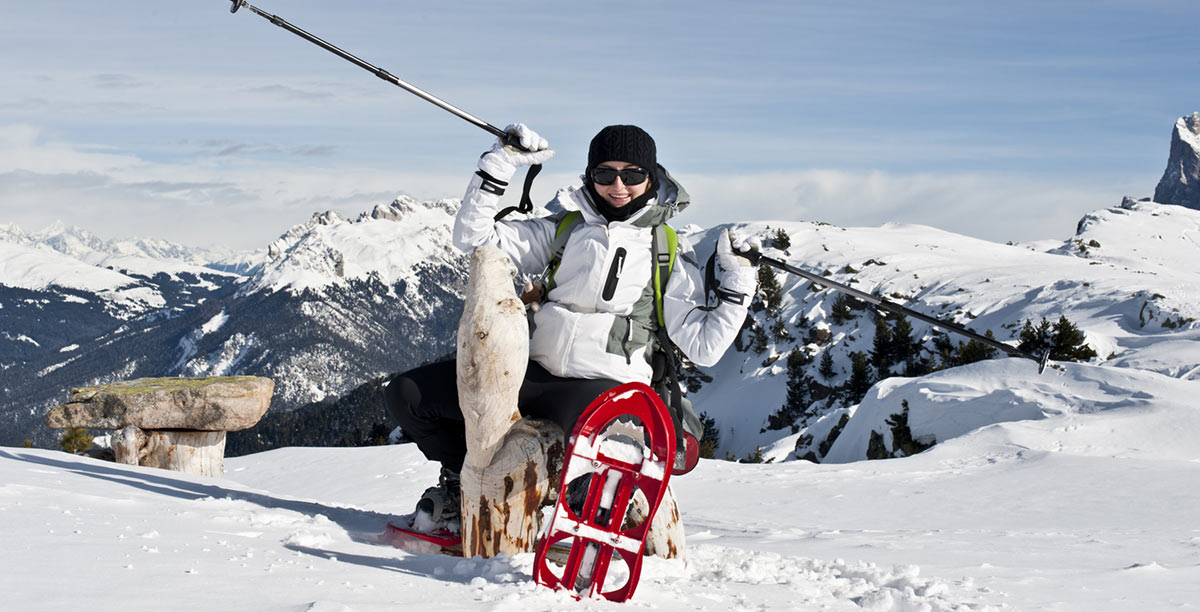 Frau mit weißer Jacke und schwarzem Hut zeigt ihre roten Schneeschuhe