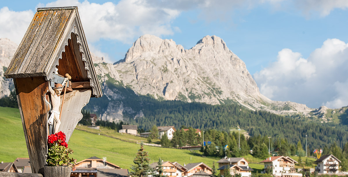 Hölzernes Kruzifix mit roten Geranien und Südtiroler Berge im Hintergrund