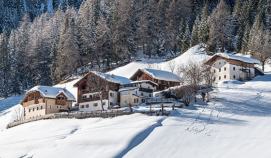Ausblick auf einige Höfe in Corvara im Winter in der verschneiter Landschaft