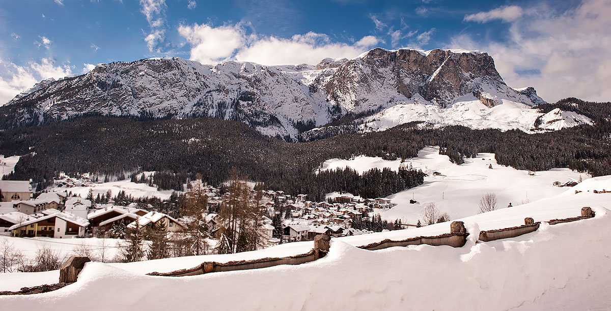 Das Dorf von Pedraces mit schneebedeckten Bergen im Hintergrund und einem Holzzaun im Vordergrund