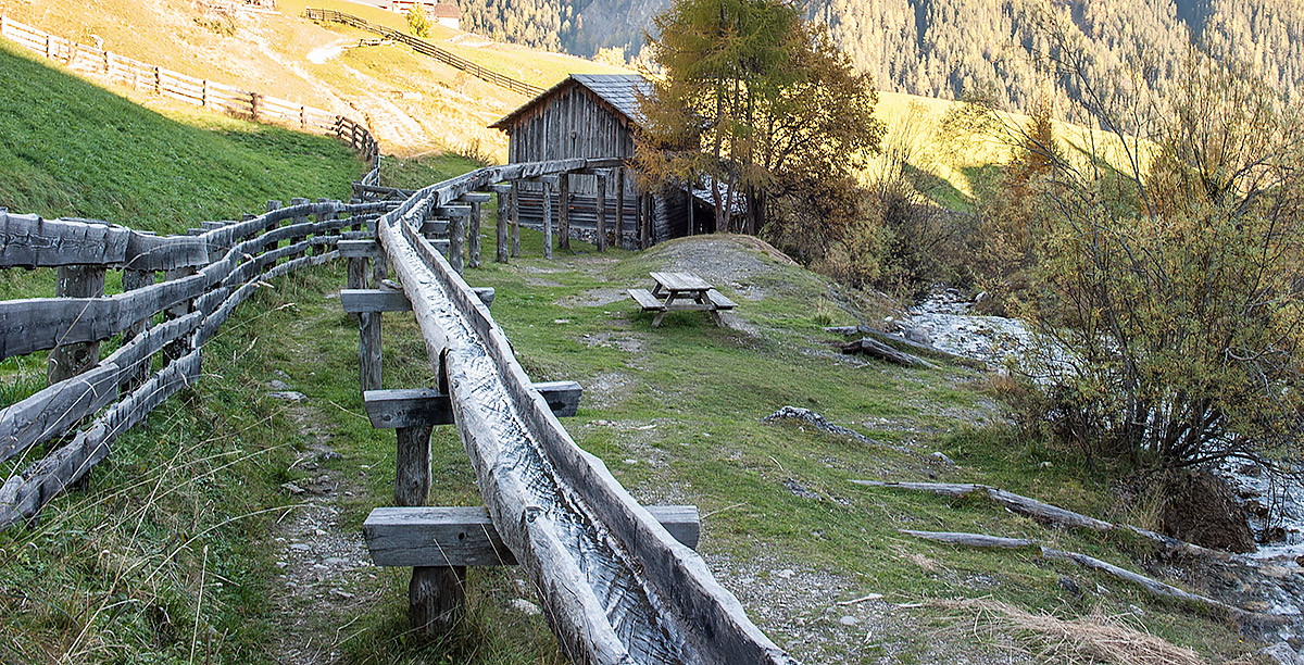 Ein  Wasserkanal in Holz in der Nähe von einem kleinen Bauernhof in Alta Badia