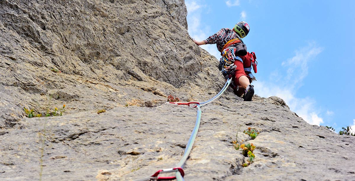 Person climbs a rock wall with safety rope attached to the wall with snap