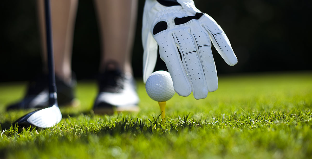 Mann mit Handschuh legt einen Golfball auf das Spielfeld
