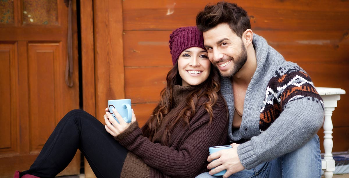 Mann und Frau vor einer Holzhütte mit Tasse in der Hand