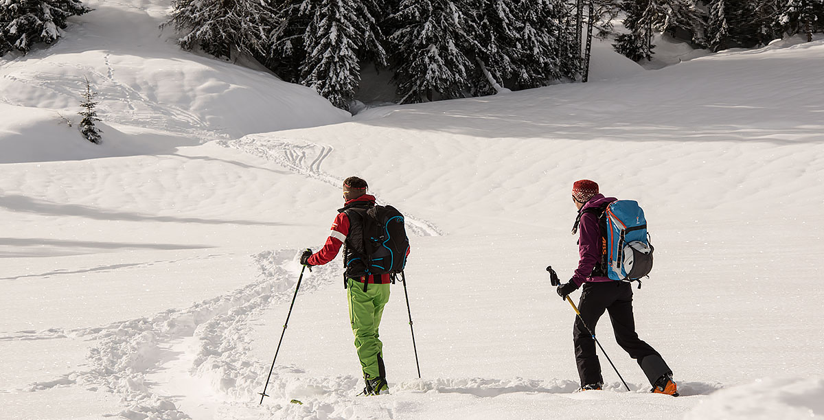 Ein Mann und eine Frau in Winterkleidung gekleidet beim Tourengehen auf einer verschneiten Wiese