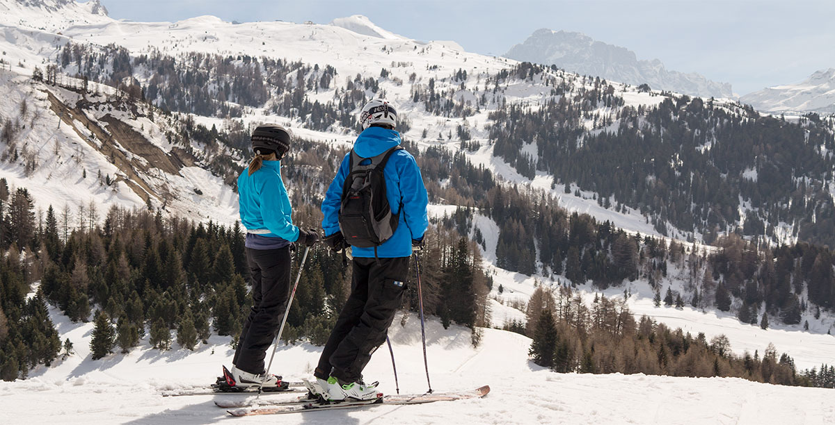 Un uomo e una donna con gli sci vestiti con giacche blu guardano il panorama