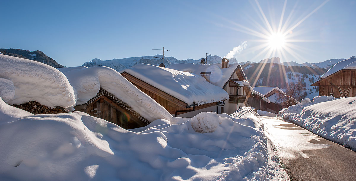 Eine Straße mit Schnee an beiden Seiten im Dorf La Valle mit glänzender Sonne